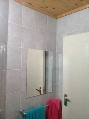 Ein Badezimmer mit grauen Fliesen, einer Holzbalkendecke, einer weißen Tür und einem Spiegel.