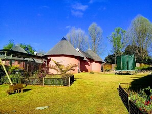 A traditional thatched-roof house with a pink exterior, surrounded by a well-maintained garden with various plants and a wooden fence. - Horizon View Chalets (Graskop)