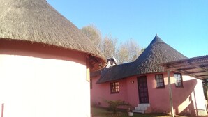 Il s’agit d’un bâtiment traditionnel à toit de chaume, dont la façade est peinte en rose, qui possède un petit porche à l’avant et un escalier apparent menant à l’entrée.