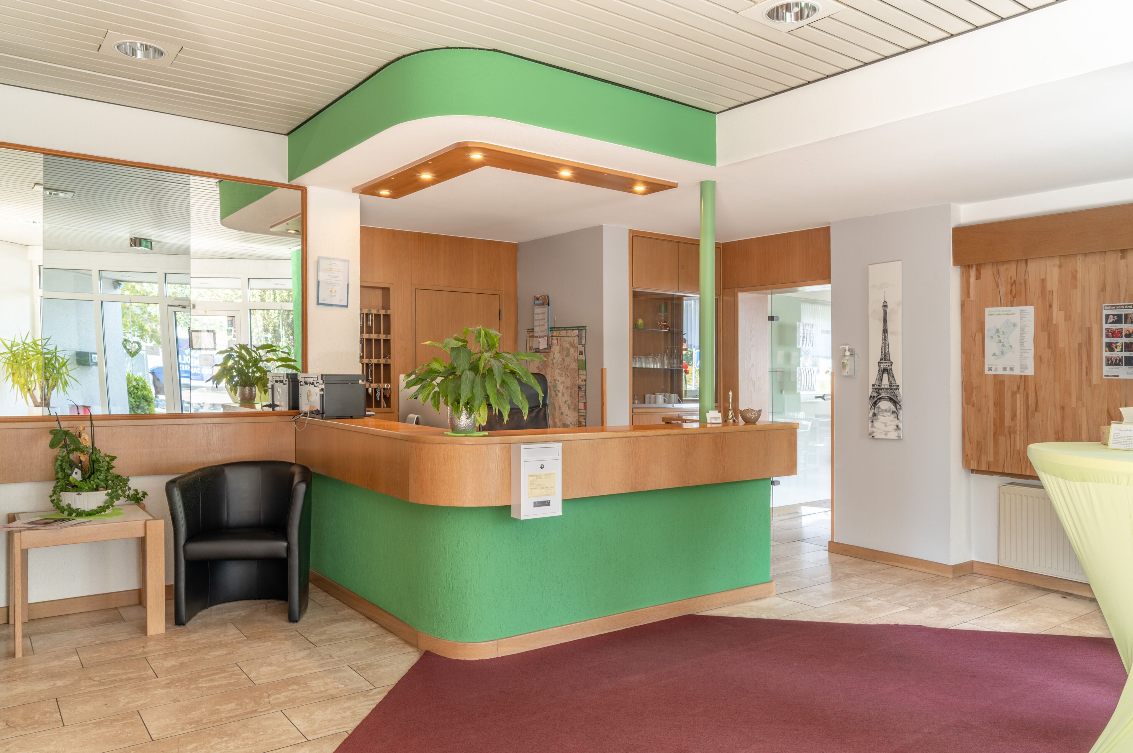 Un'area reception con un bancone verde, mobili in legno, una sedia nera e una pianta in vaso.