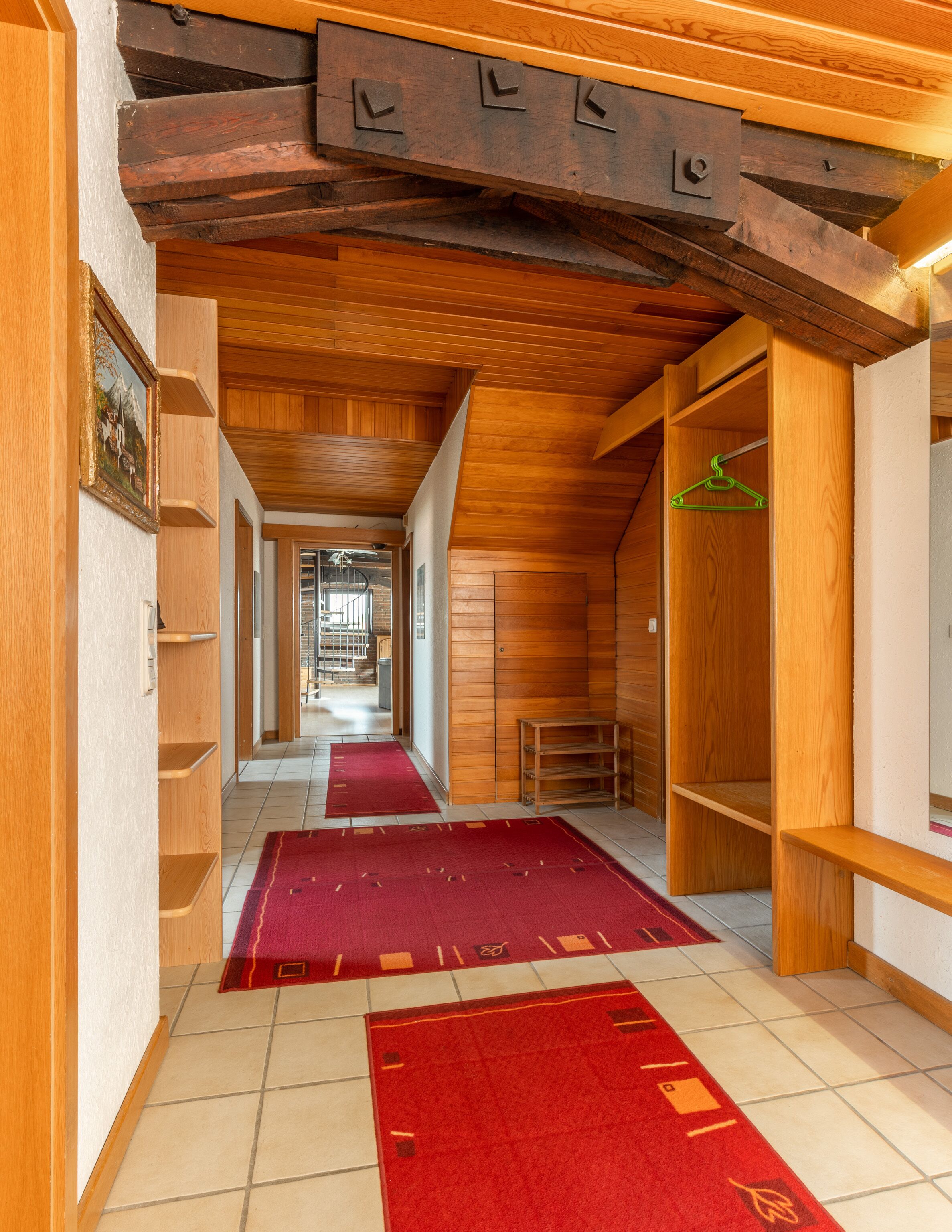 Un pasillo con vigas de madera, alfombras rojas y un perchero de madera.