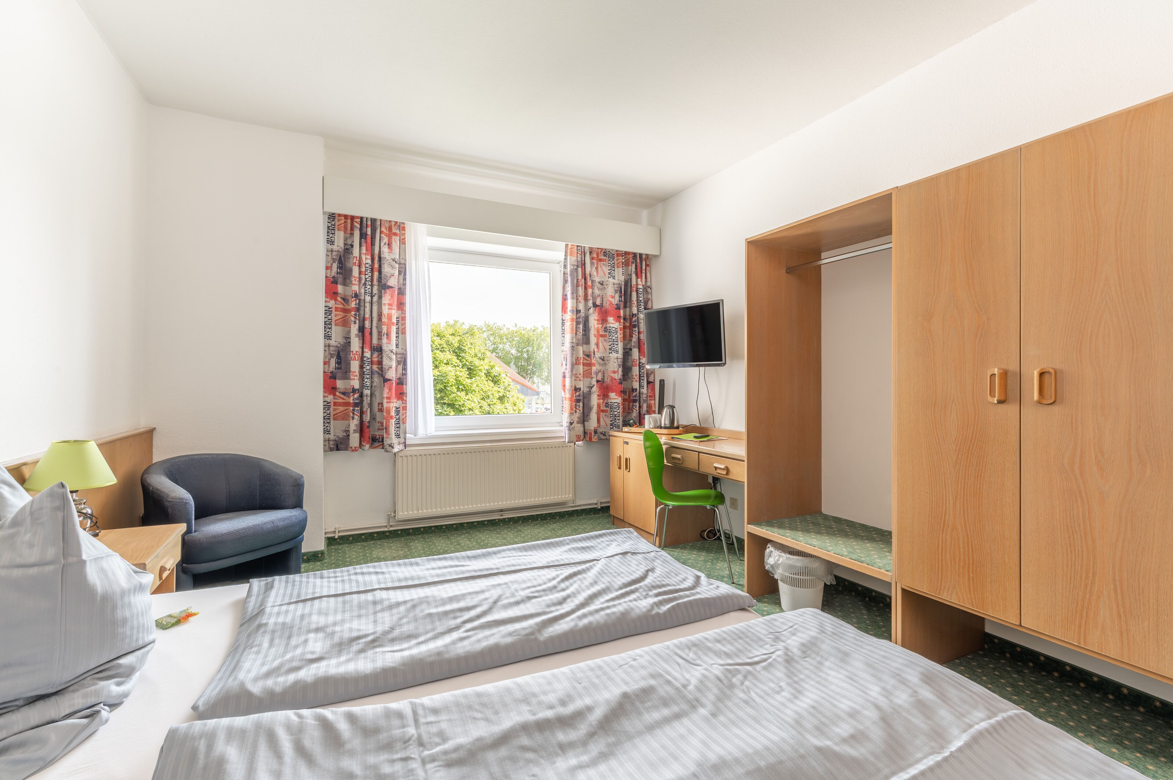 A hotel room with two beds, a desk, a chair, a TV, and a wardrobe.