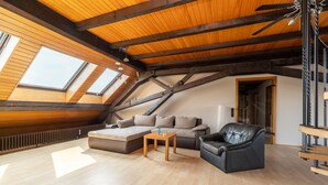 Un espacio tipo loft con techo inclinado, vigas de madera, un sofá, un sillón de cuero y una pequeña mesa.