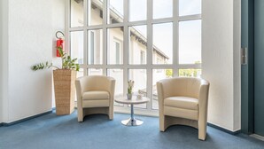 Una habitación con dos sillones color beige, una mesita redonda con un florero, una cesta de mimbre y un extintor rojo en la pared.