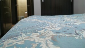 A bed with a floral patterned bedspread, a dark wooden wardrobe, and a door leading to another room. - Welcome Home 20 (Tashkent)