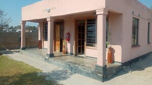 A pink building with a covered entrance, columns, and potted plants. - Little Lodge (Choma)