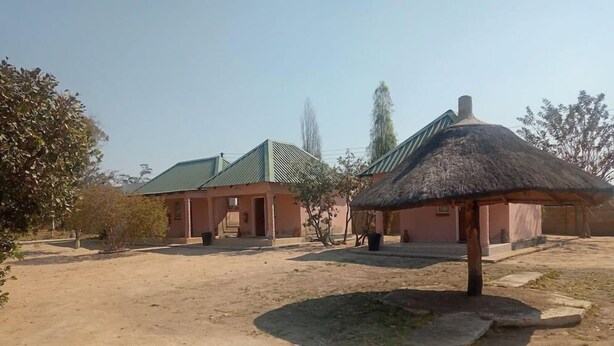 A building with a green roof and a thatched-roof structure in a courtyard. - Little Lodge (Choma)