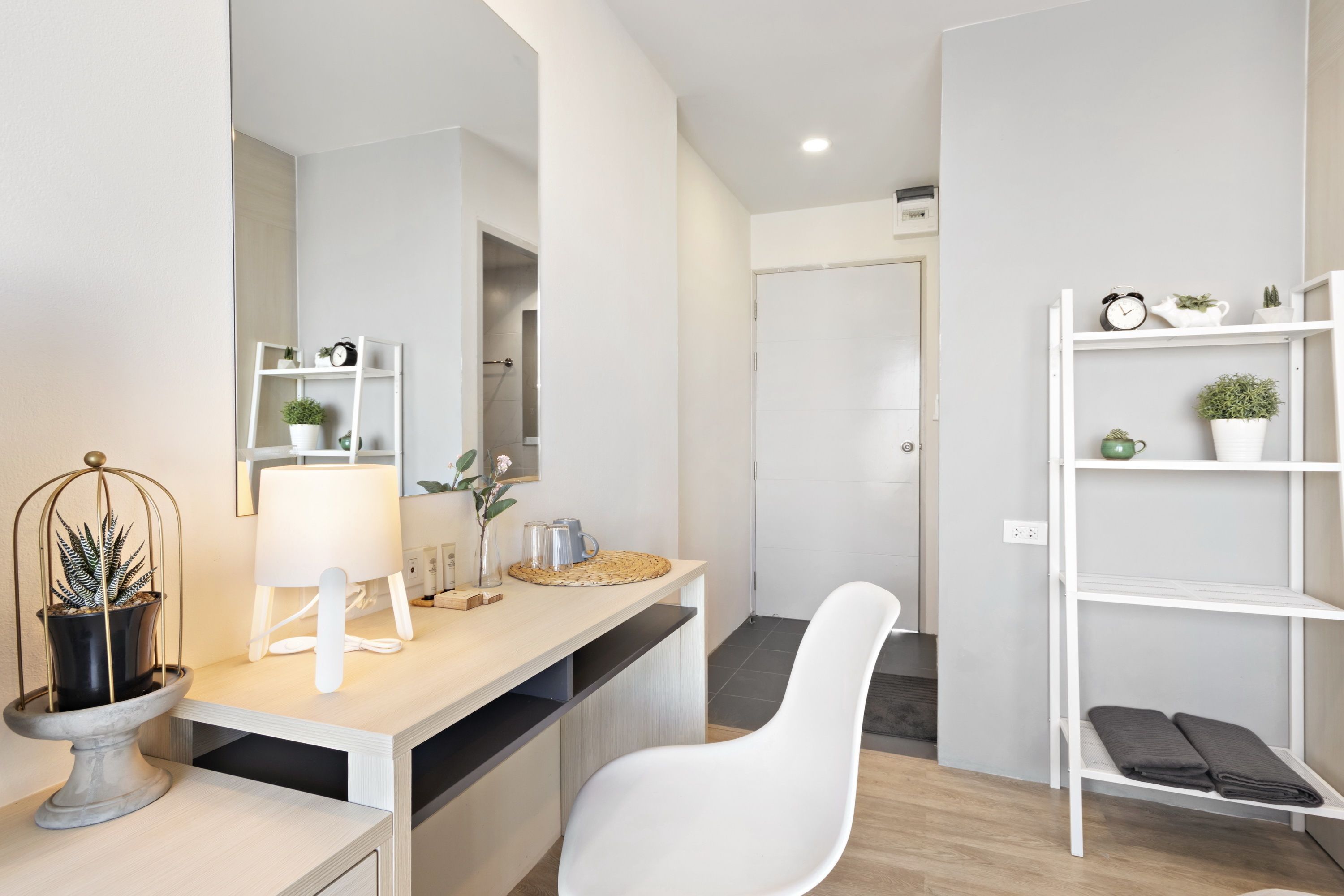 A modern bathroom with a white vanity, a mirror, and a white chair. There is a shelf with plants and a towel rack.