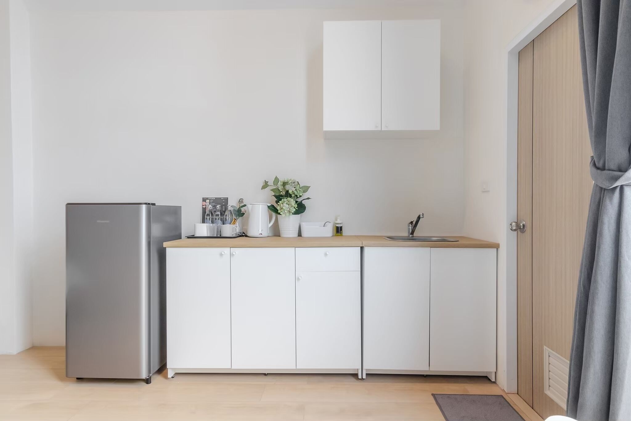 A compact kitchen with white cabinets, a stainless steel refrigerator, and a wooden countertop.