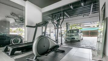 Un gimnasio con equipo de ejercicio, un coche al fondo y vistas al exterior a través de amplias ventanas.