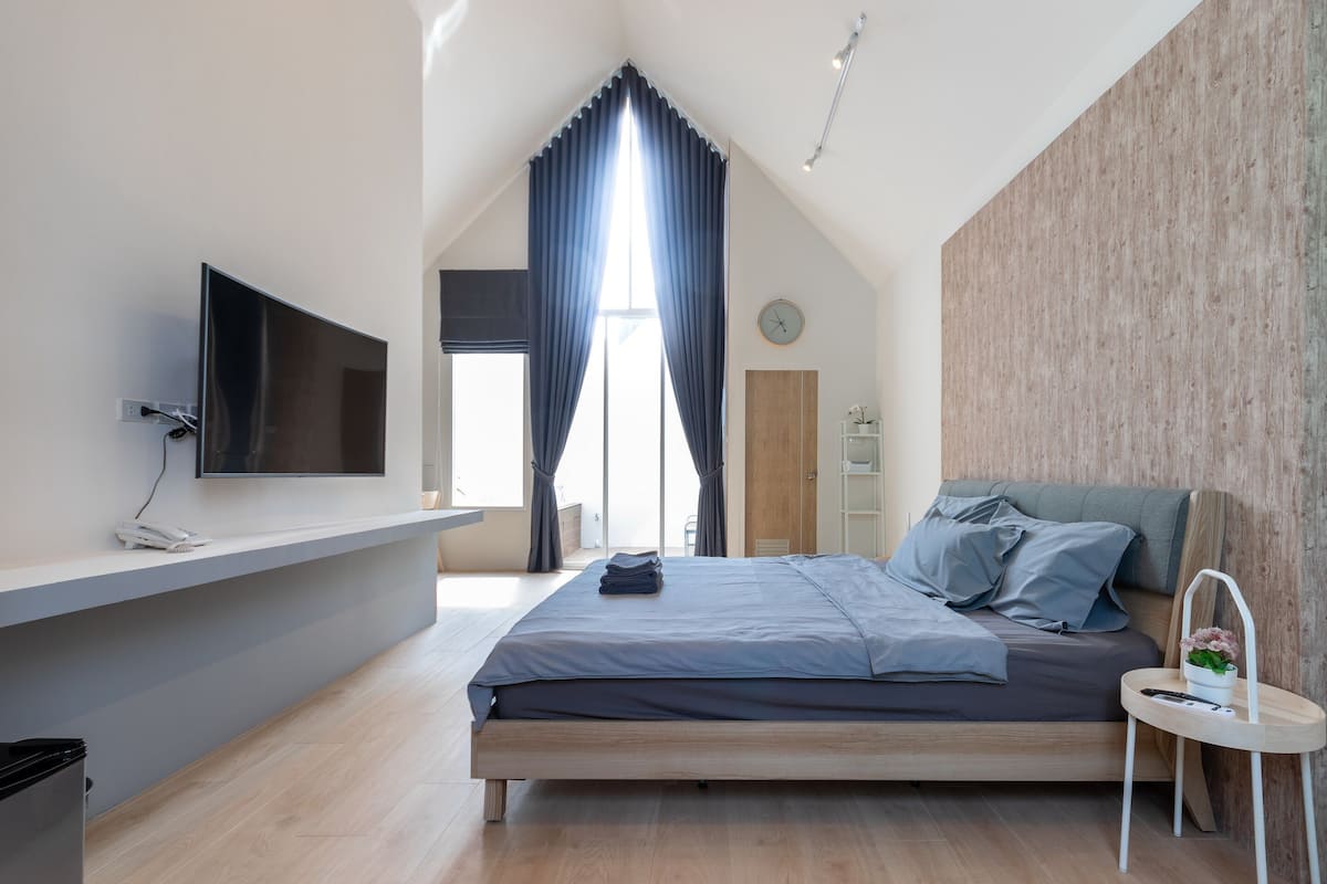 A modern bedroom with a bed, a TV mounted on the wall, a small bedside table, and a window with curtains.