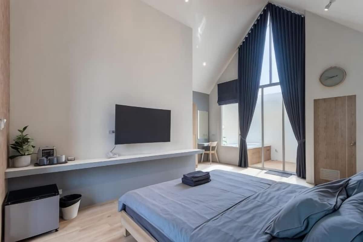 A modern bedroom with a bed, a mounted TV, a desk, and a large window with curtains.
