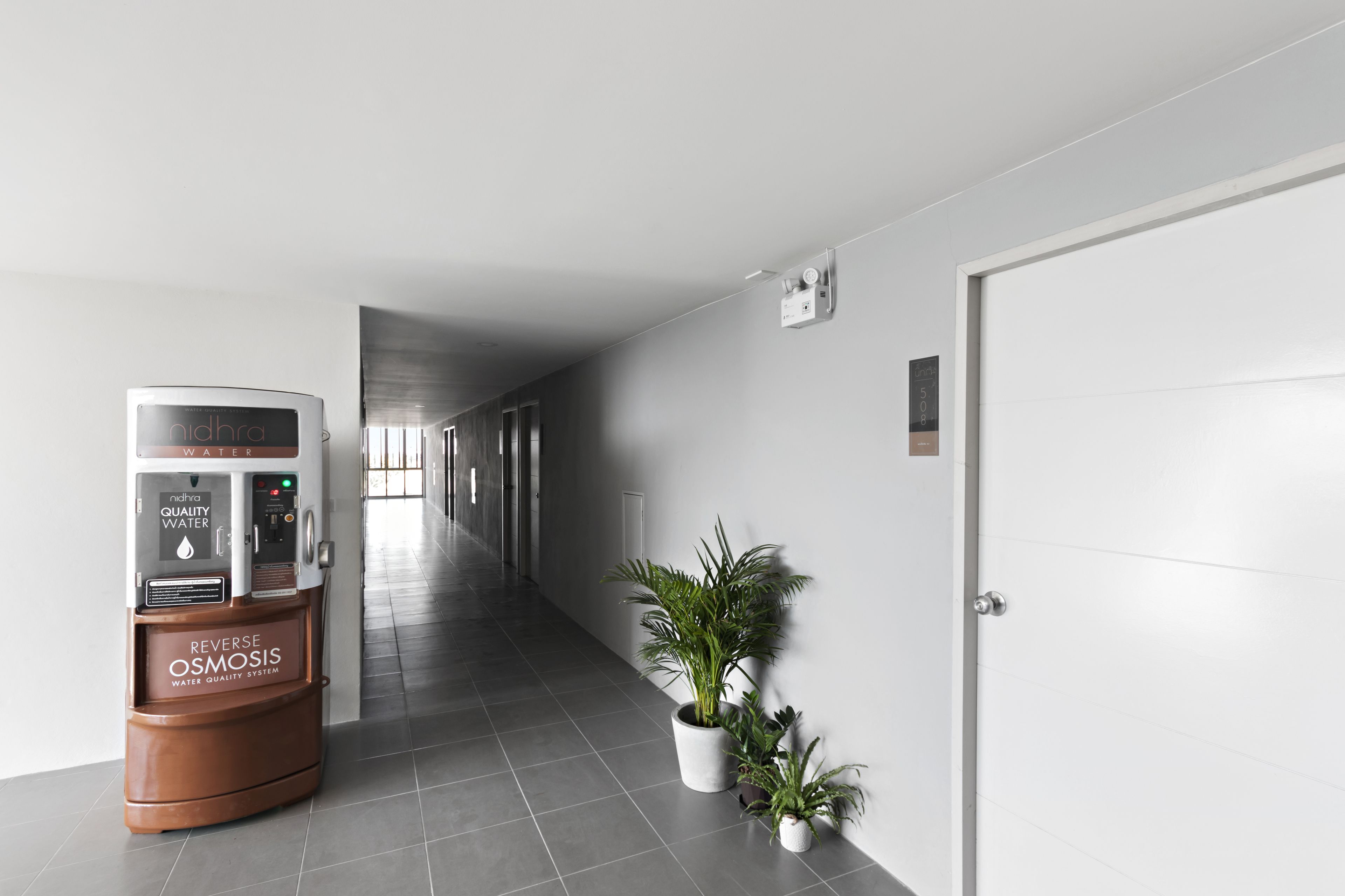 A hallway with a water dispenser, potted plants, and a door.