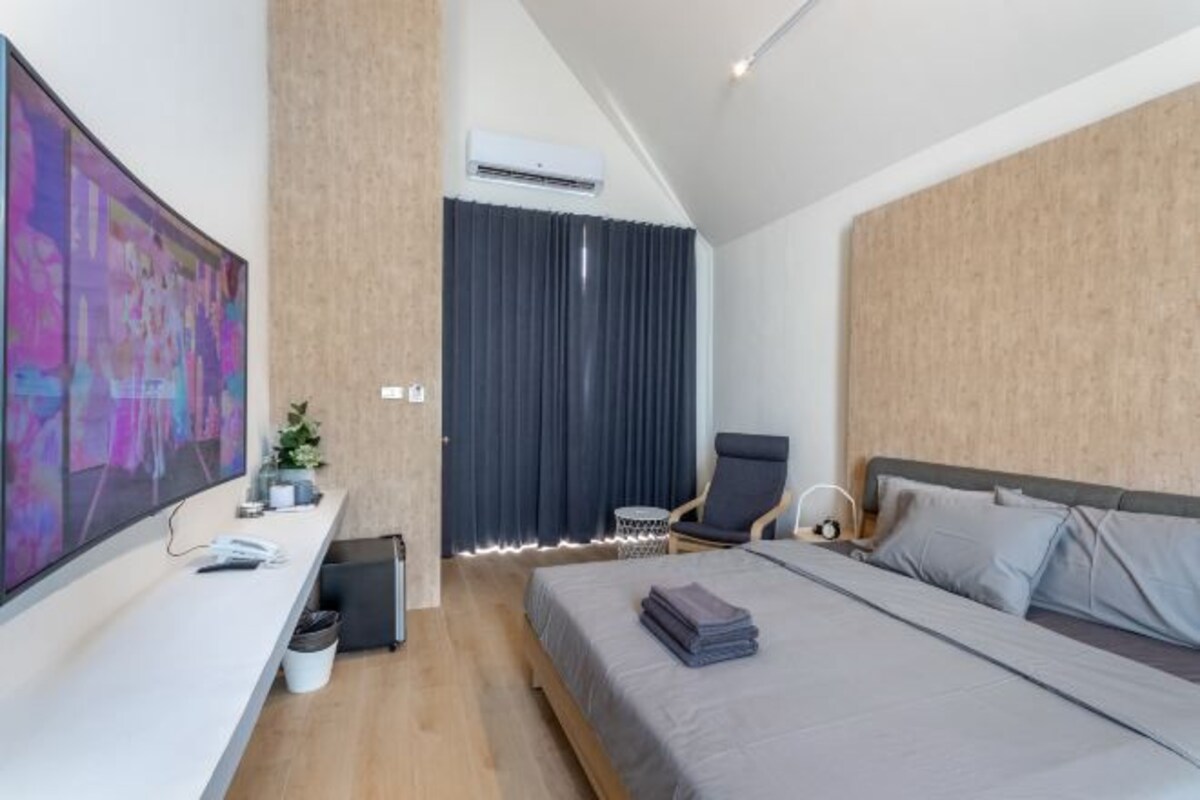 A modern hotel room with a large bed, a desk with a flat-screen TV, a chair, and a window with curtains.