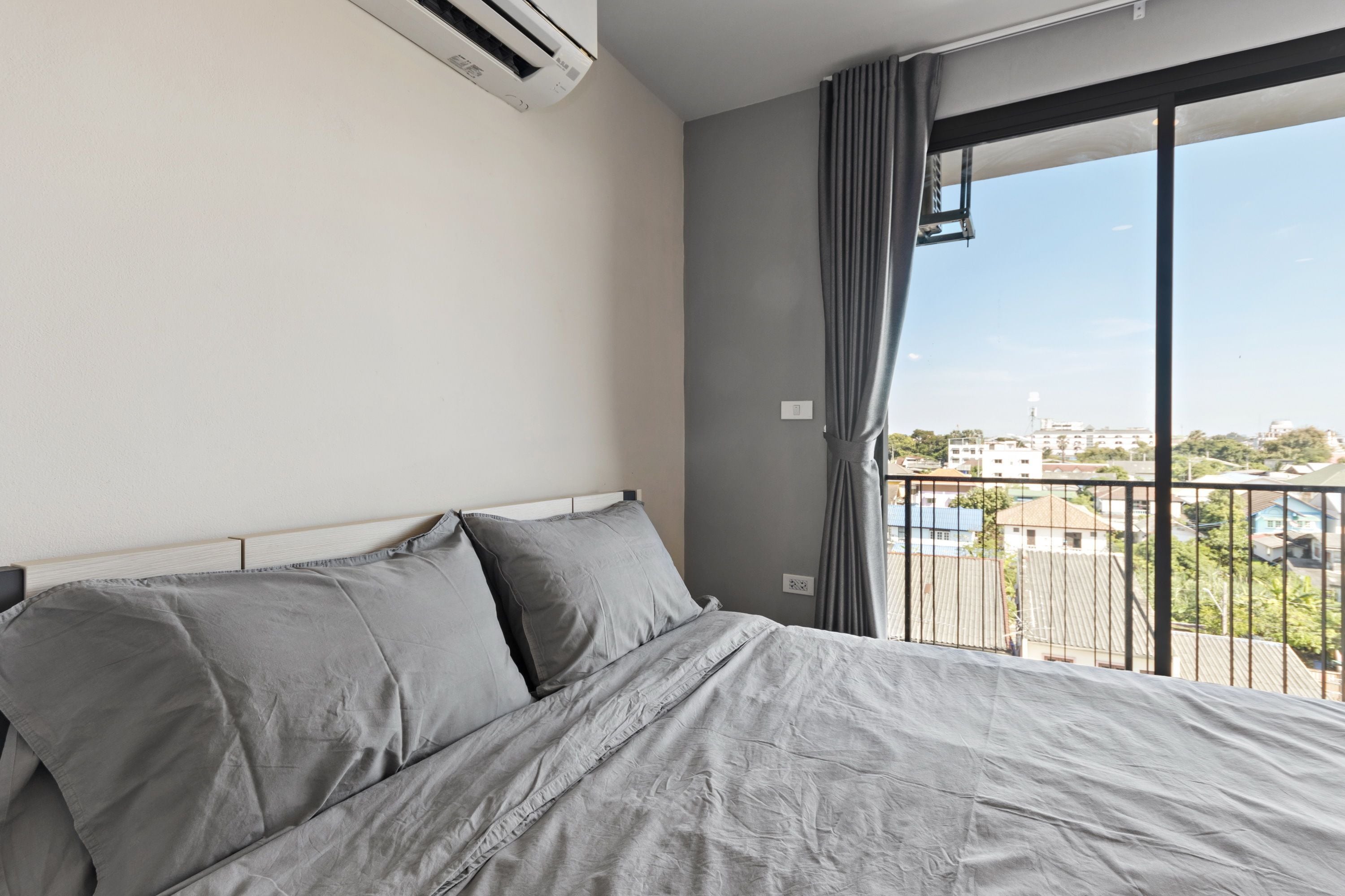 Une chambre d’hôtel avec un lit, un appareil de climatisation, une fenêtre avec des rideaux et une vue sur les bâtiments environnants.