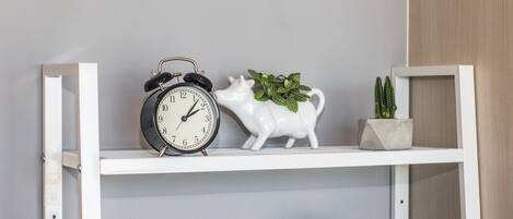 Una repisa con un reloj, un cerdito de cerámica y dos macetas.