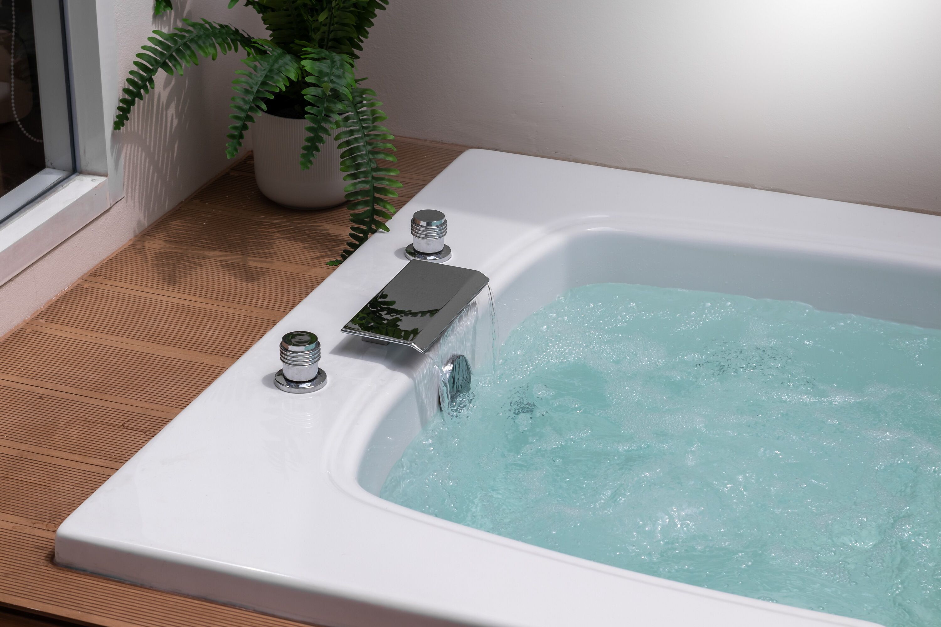 Un baño moderno con una bañera blanca, un helecho en maceta y suelo de madera.