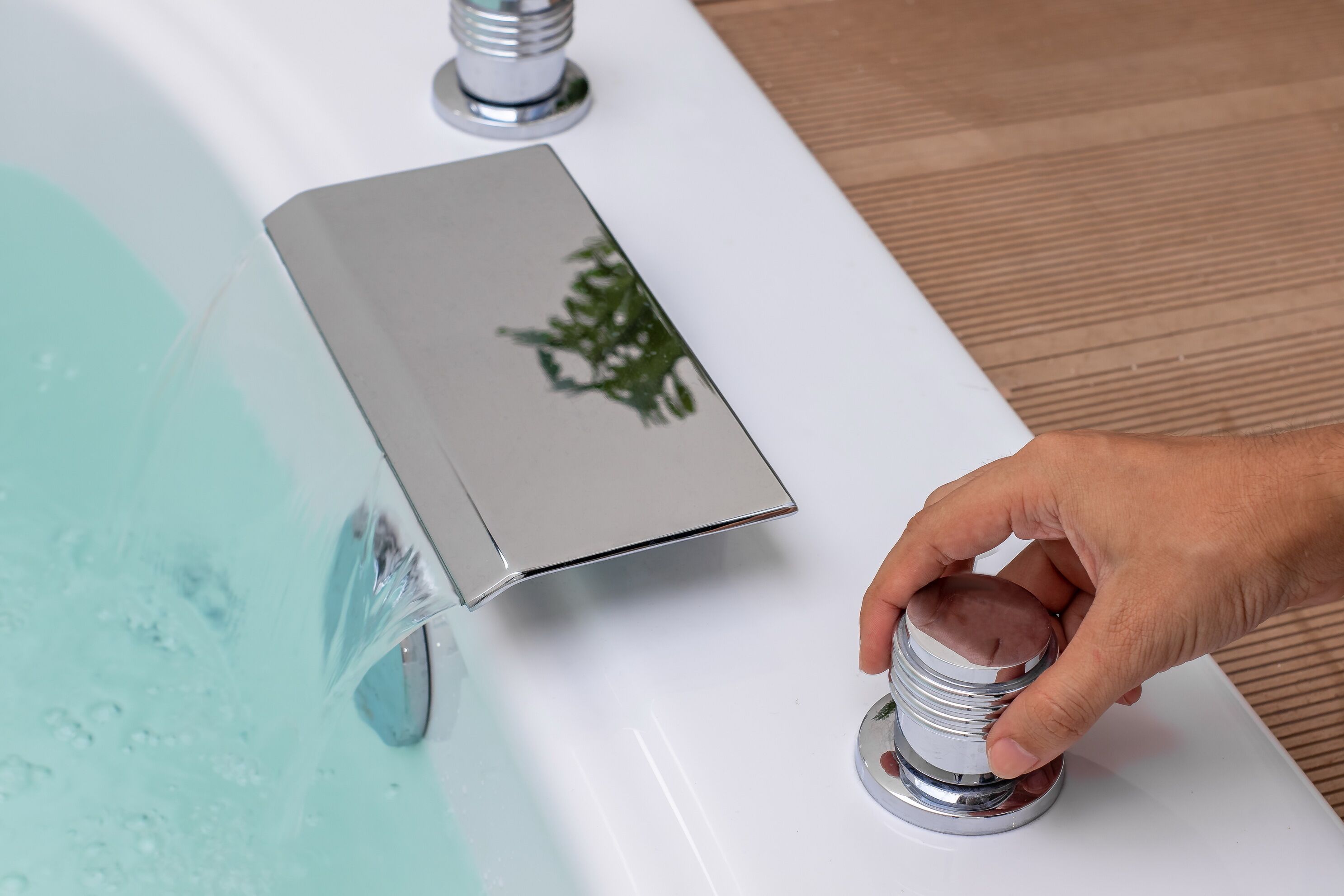 A hand adjusting a faucet on a white bathtub.