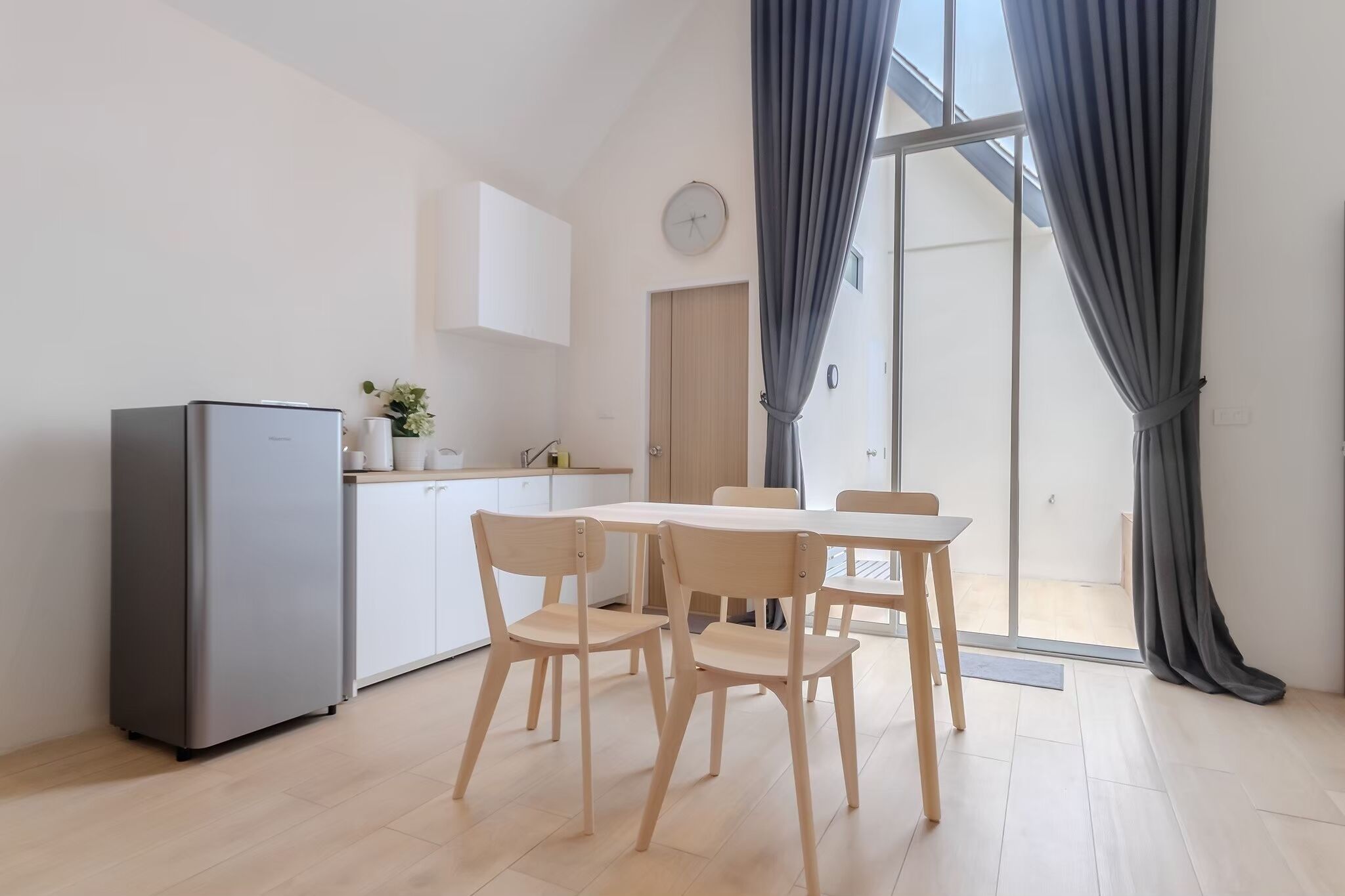 A modern kitchen with a refrigerator, cabinets, and a dining area with chairs and a table.