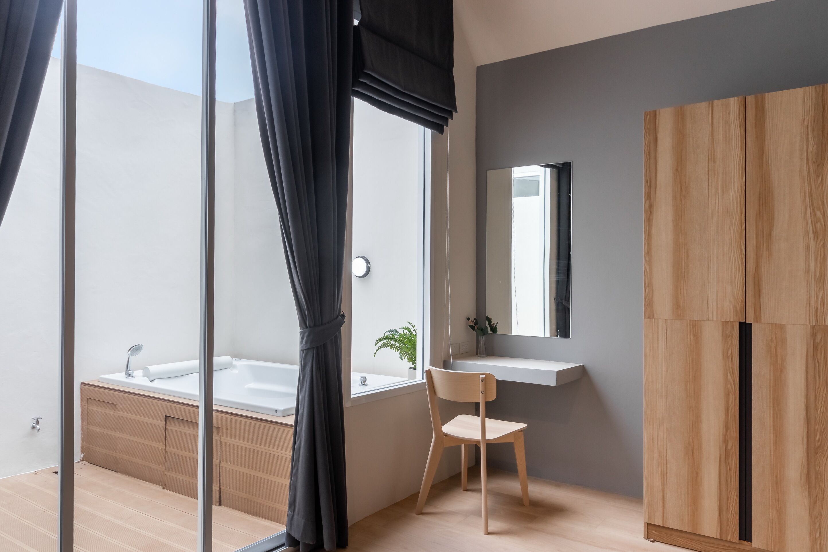 A modern bathroom with a bathtub, a wooden chair, a sink, and a mirror.