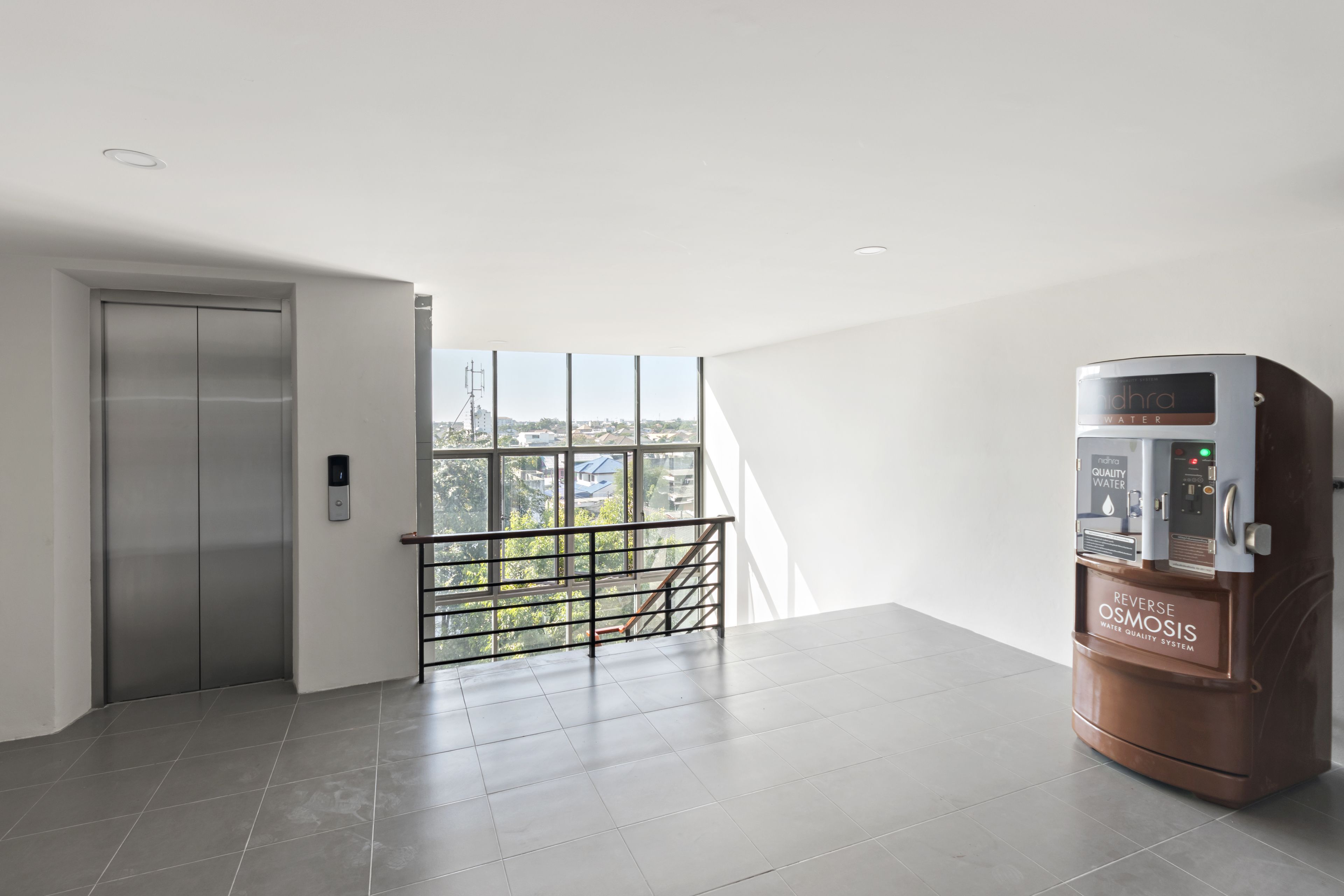 Una habitación de hotel moderna con un ventanal grande, dispensador de agua y un ascensor.