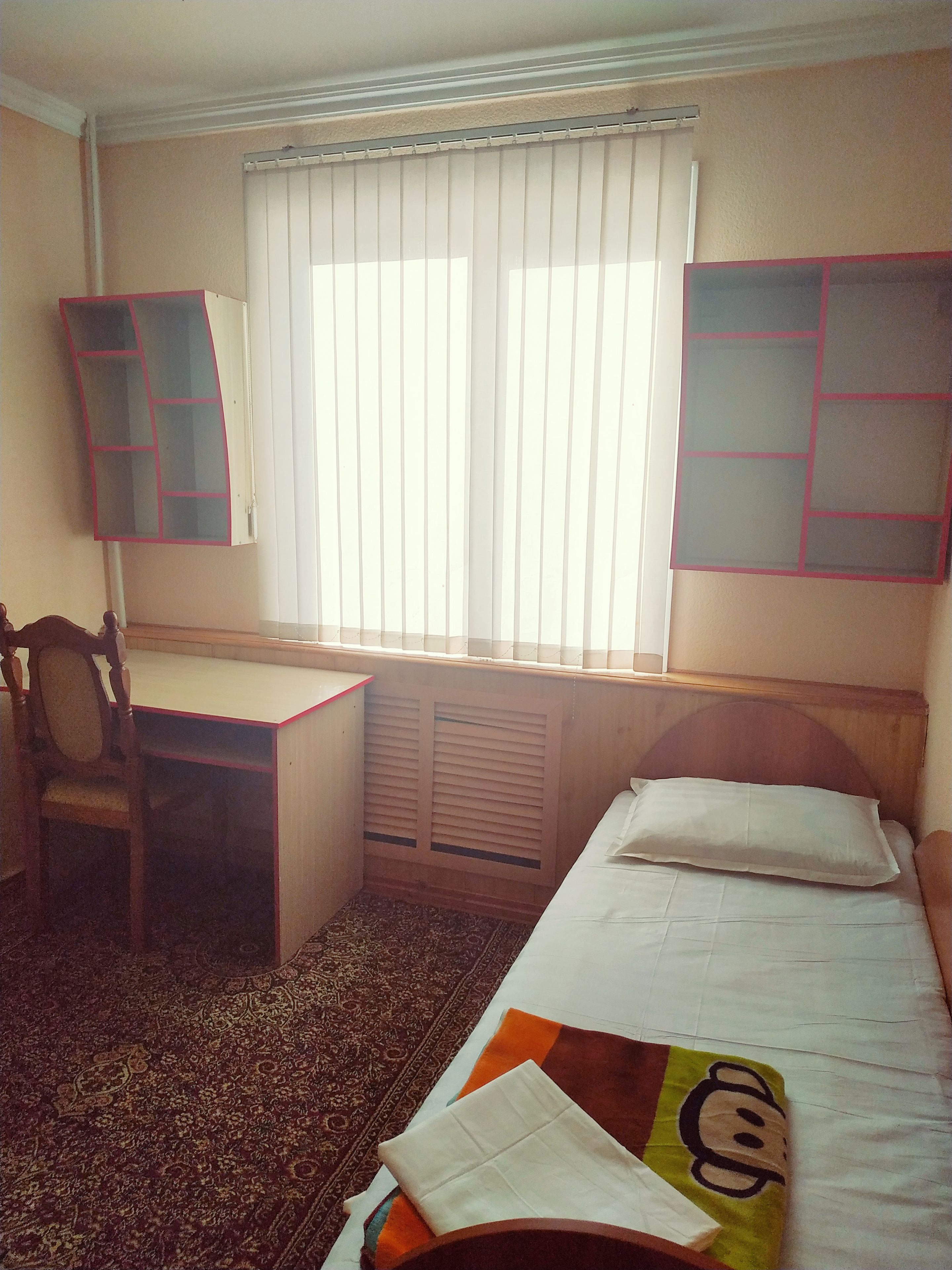 Une chambre d’hôtel avec un lit simple, un bureau et une chaise.
