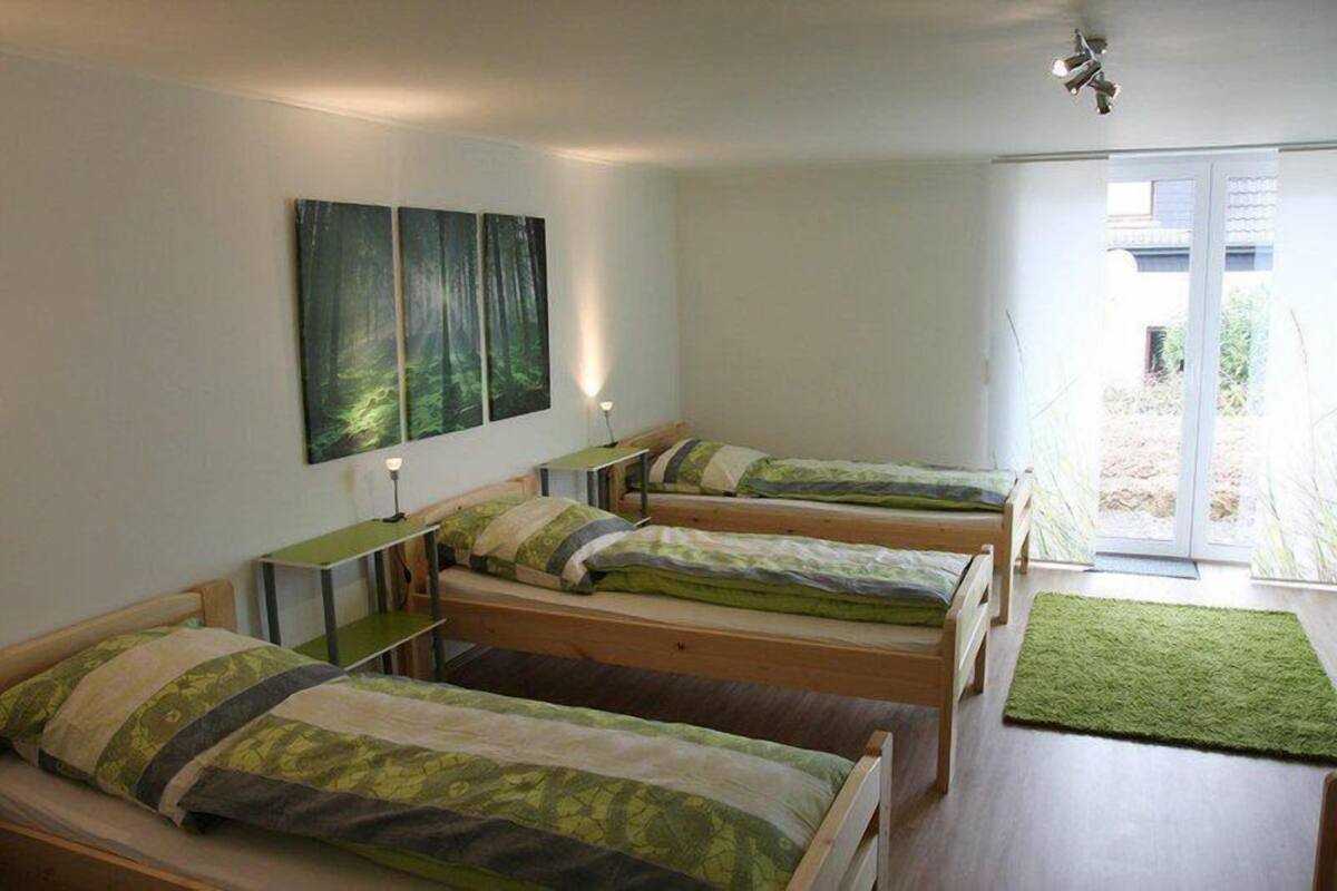 A dormitory room with four single beds, a desk, and a green rug.