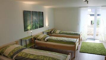 A dormitory room with four single beds, a desk, and a green rug.