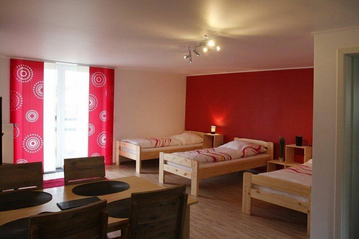 A room with two wooden beds, a dining table with chairs, and a red wall.