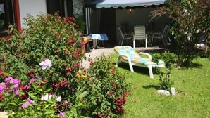 Un jardín con césped, una silla blanca y una mesa con mantel azul.