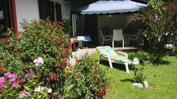 A garden with a lawn, a white chair, and a table with a blue tablecloth.