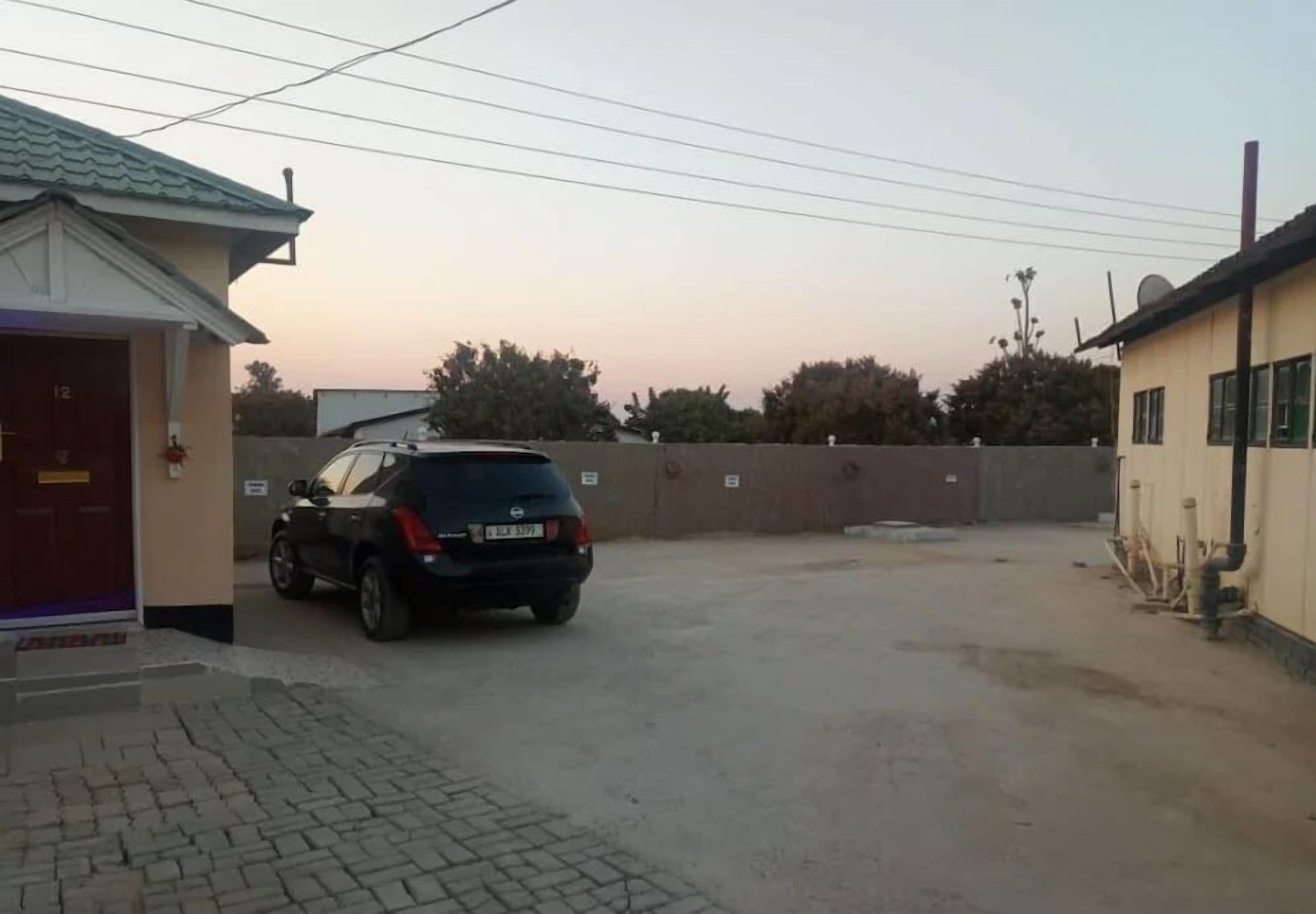 A parking area with a car, a building with a red door, and a wall with small windows.
