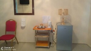 Une pièce avec une petite table, une chaise, une lampe et un réfrigérateur.