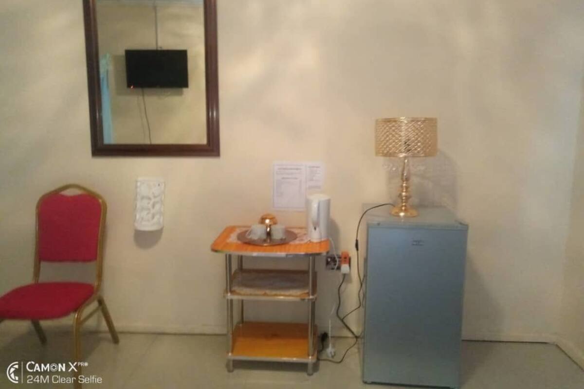 A room with a small table, a chair, a lamp, and a refrigerator.