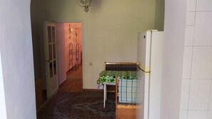 Een kleine kamer met een bed, een stoel en een koelkast. Er is een deur die naar een andere kamer leidt.