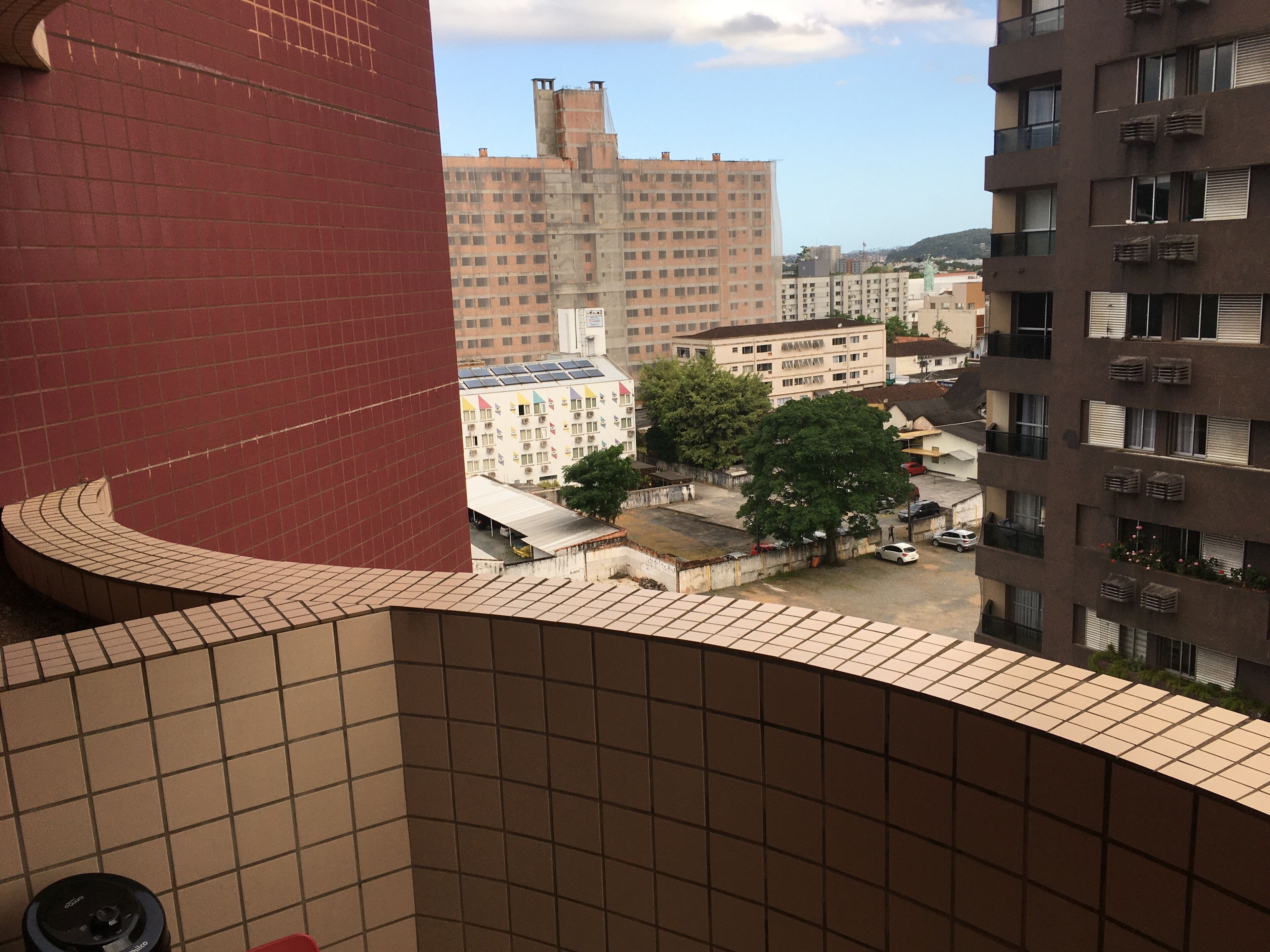A view of a building with a curved tiled facade and a large window overlooking a parking area and other buildings.