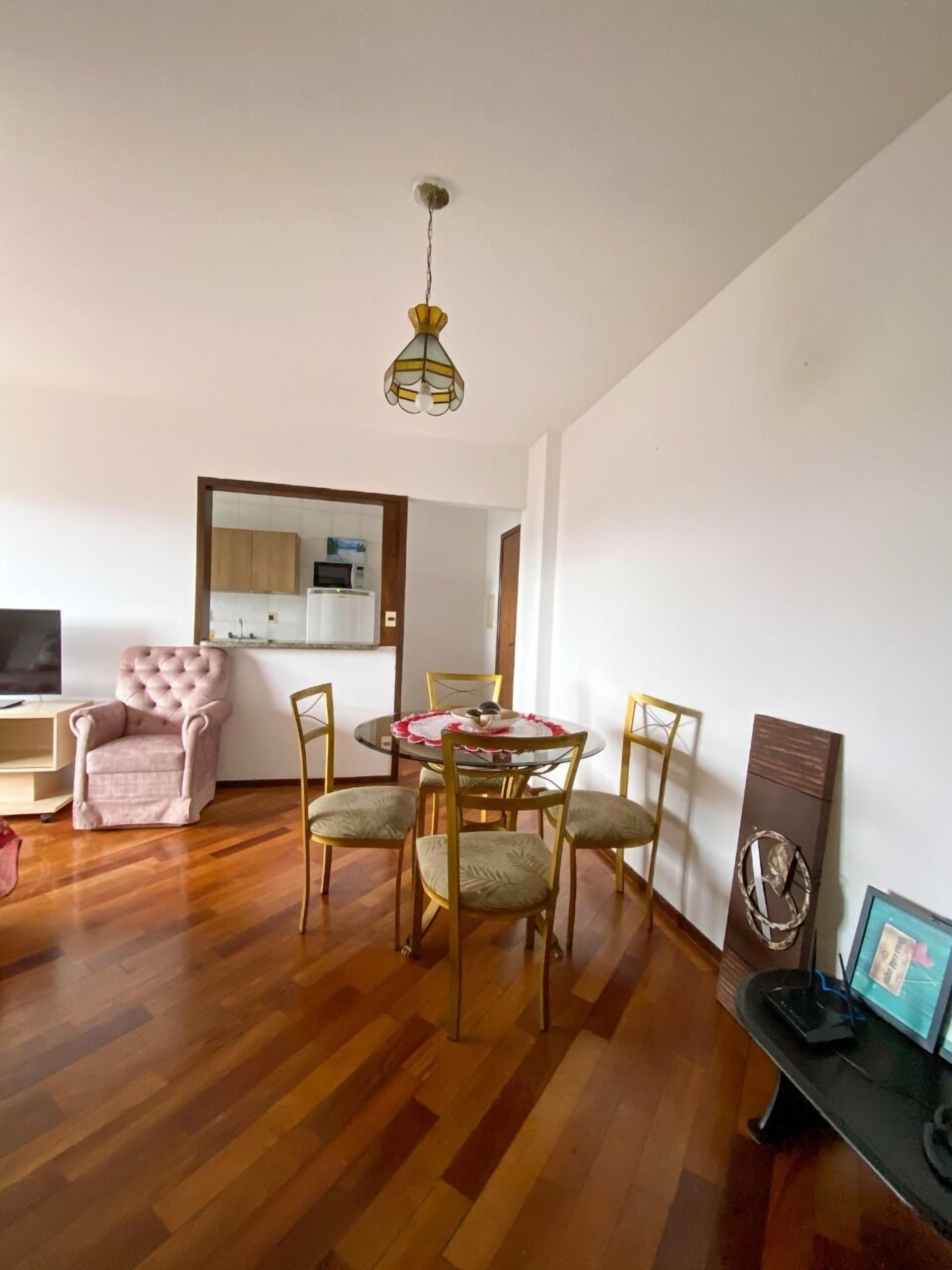 A modern living room with a dining table, chairs, a pink armchair, and a television.