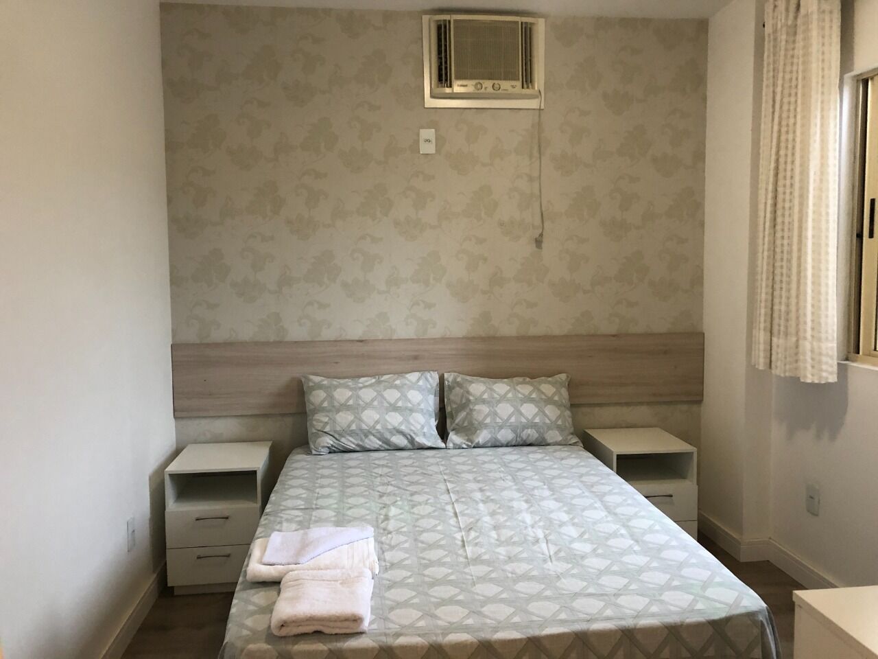 Una camera da letto con un letto, due comodini, una finestra e un condizionatore d'aria a muro.