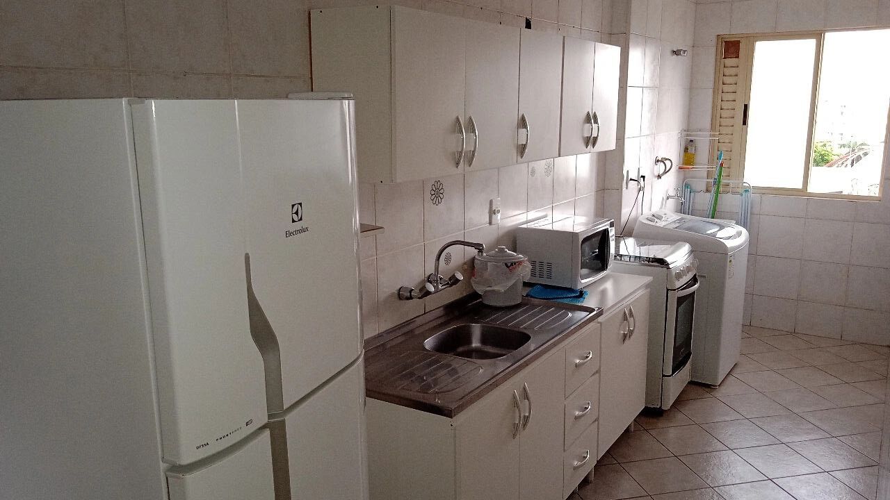 Cozinha com armários brancos, pia, micro-ondas e geladeira.