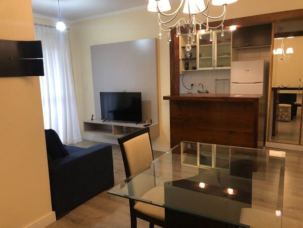 A modern living room with a glass dining table, a sofa, and a TV.