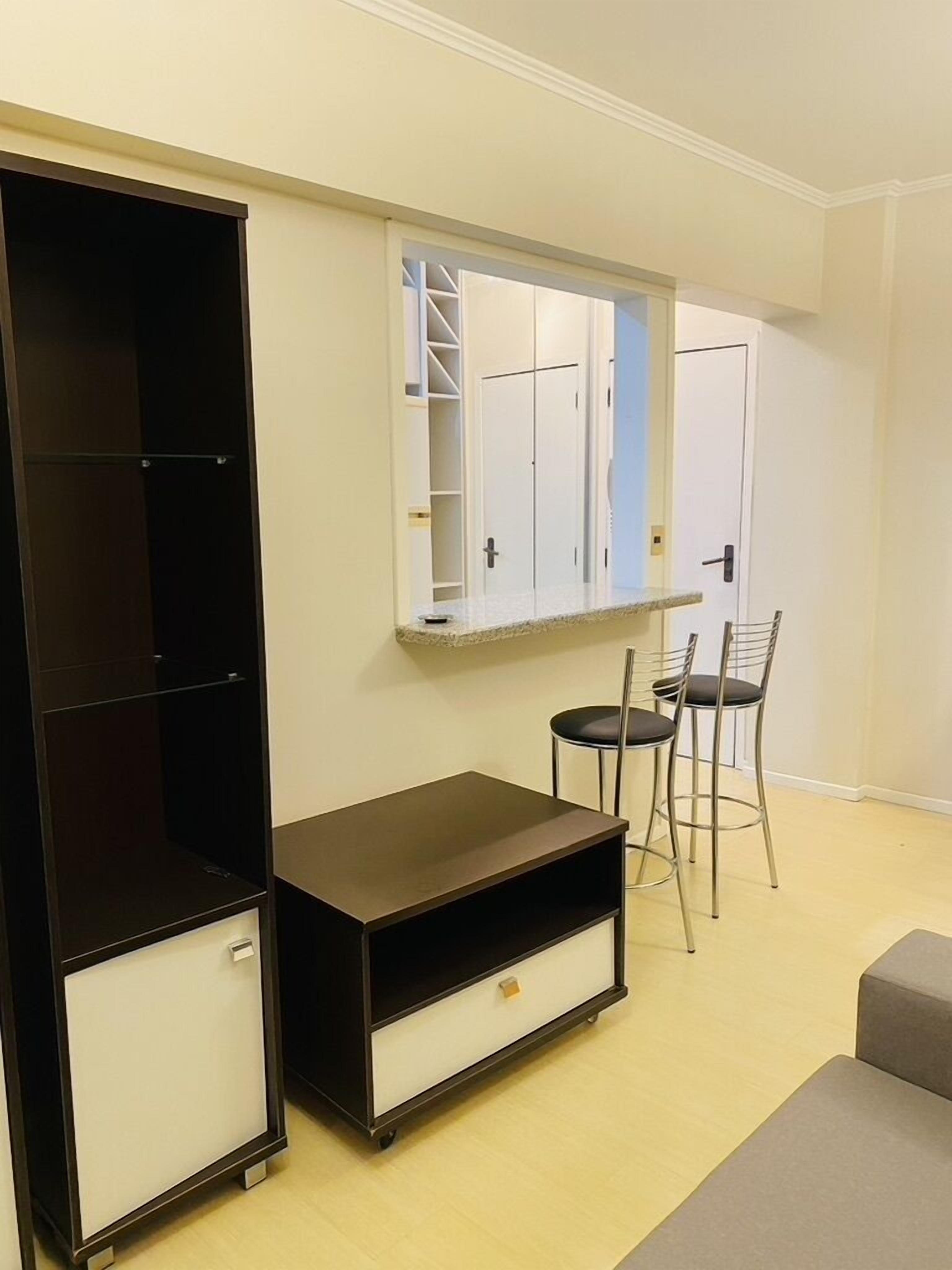 Un espacio habitable compacto con un armario oscuro, un pequeño mueble para televisión y un espejo sobre una puerta.