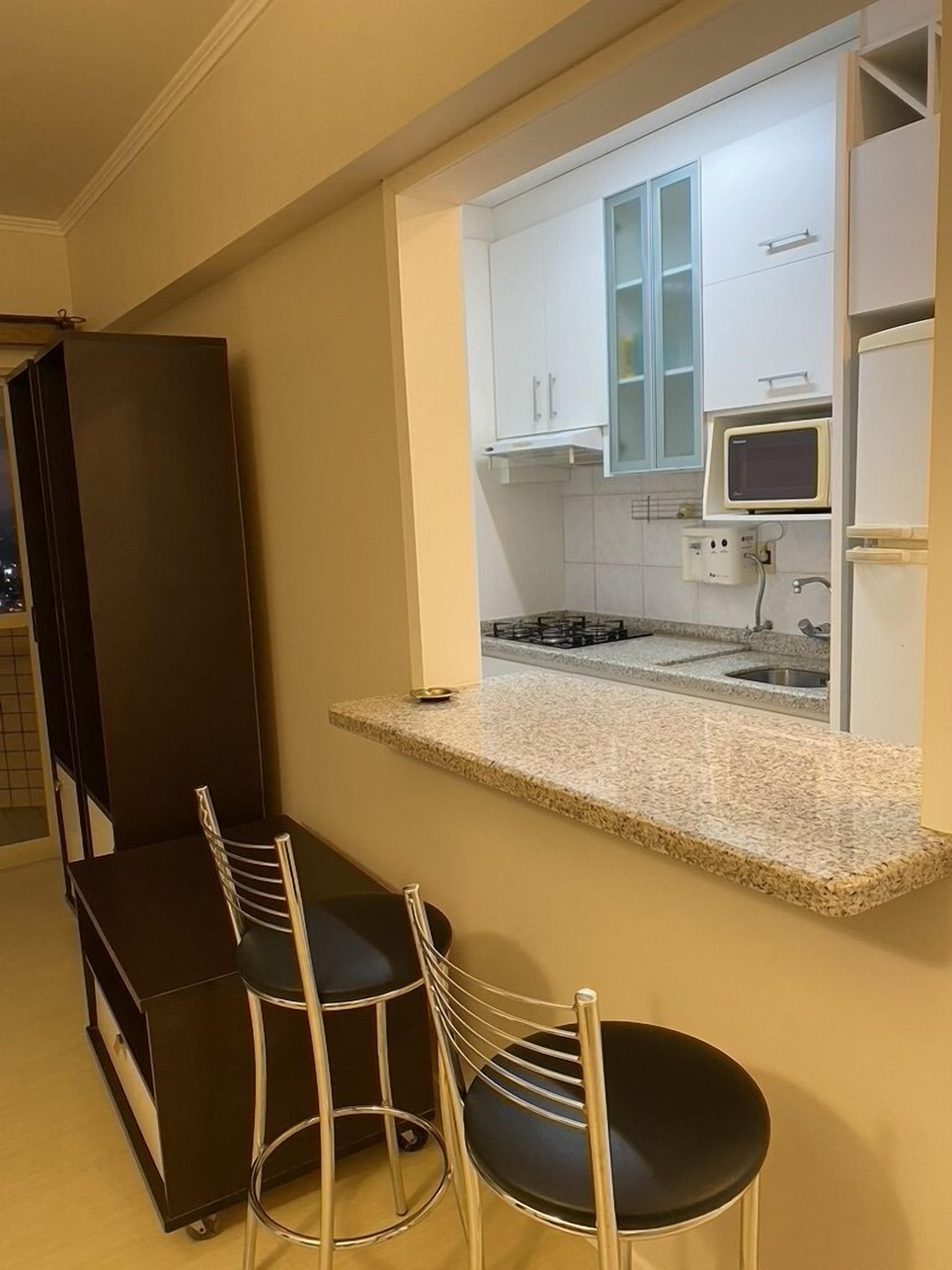 A compact kitchen with white cabinets, a microwave, and a gas stove. There are two black chairs with metal frames and a dark-colored table.