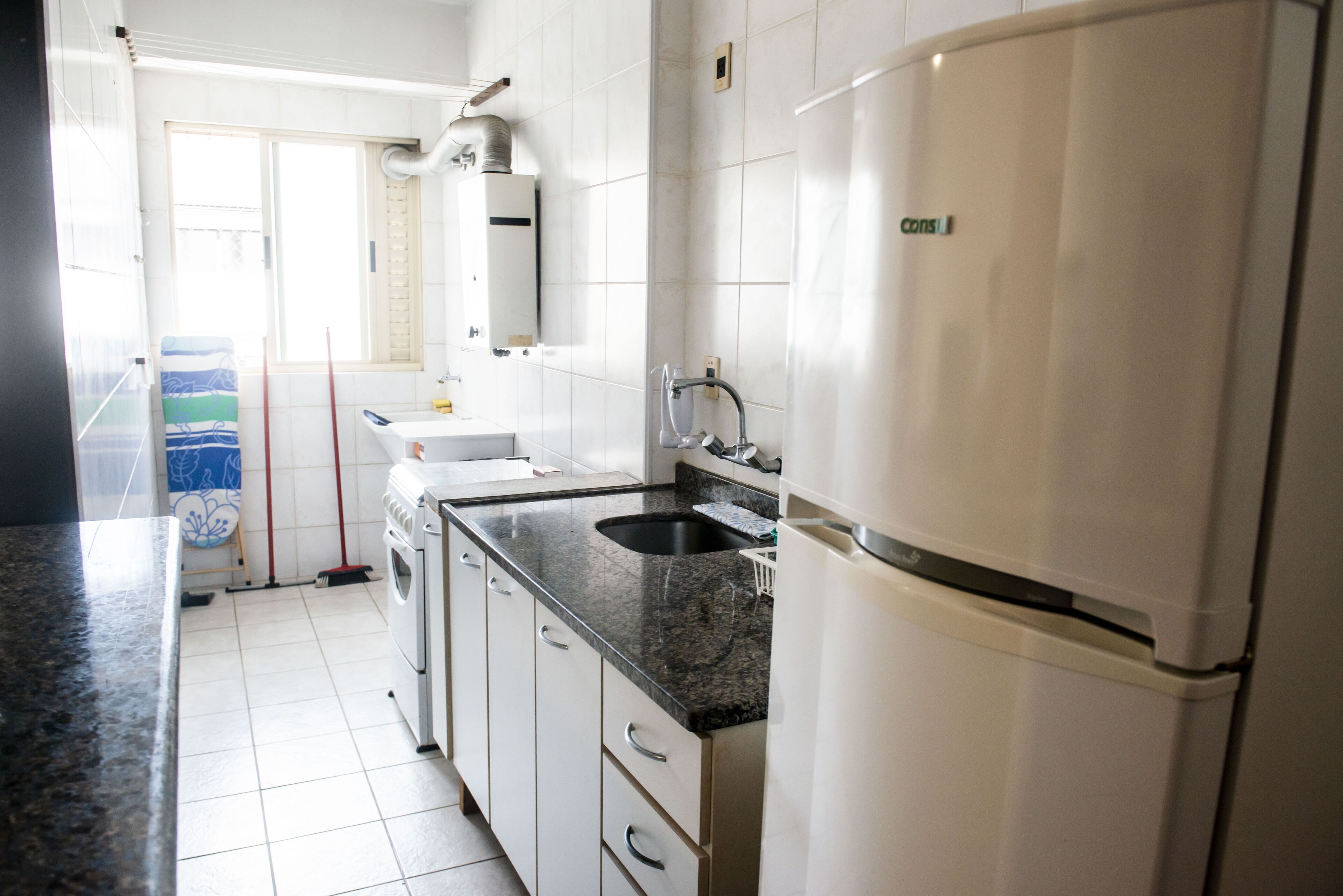A modern kitchen with white cabinets, a granite countertop, a built-in oven, and a refrigerator.