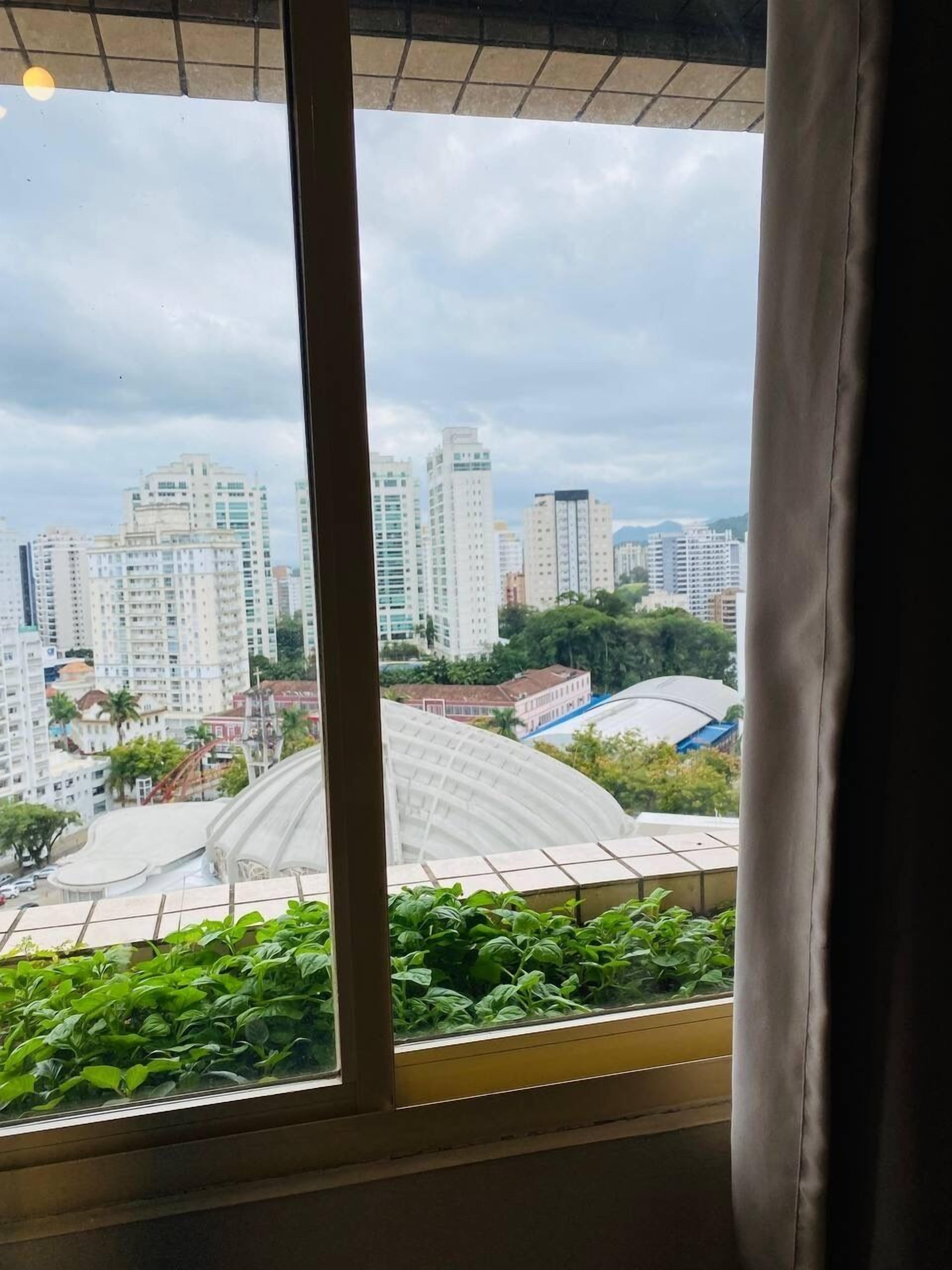 A view from a window with a curtain, overlooking a cityscape with high-rise buildings and a large dome structure.