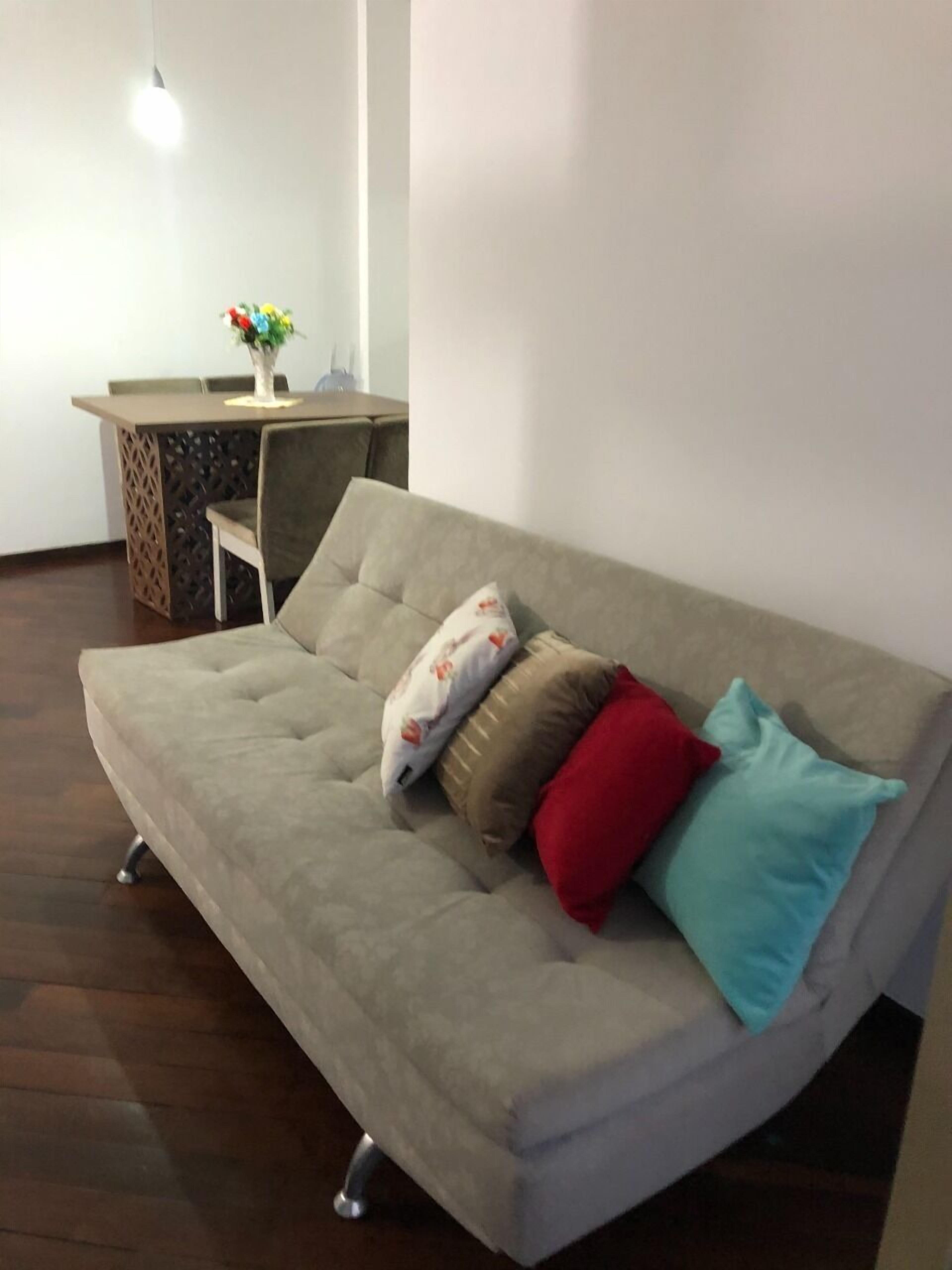 A modern living room with a grey sofa, a small dining table with chairs, and a decorative vase.