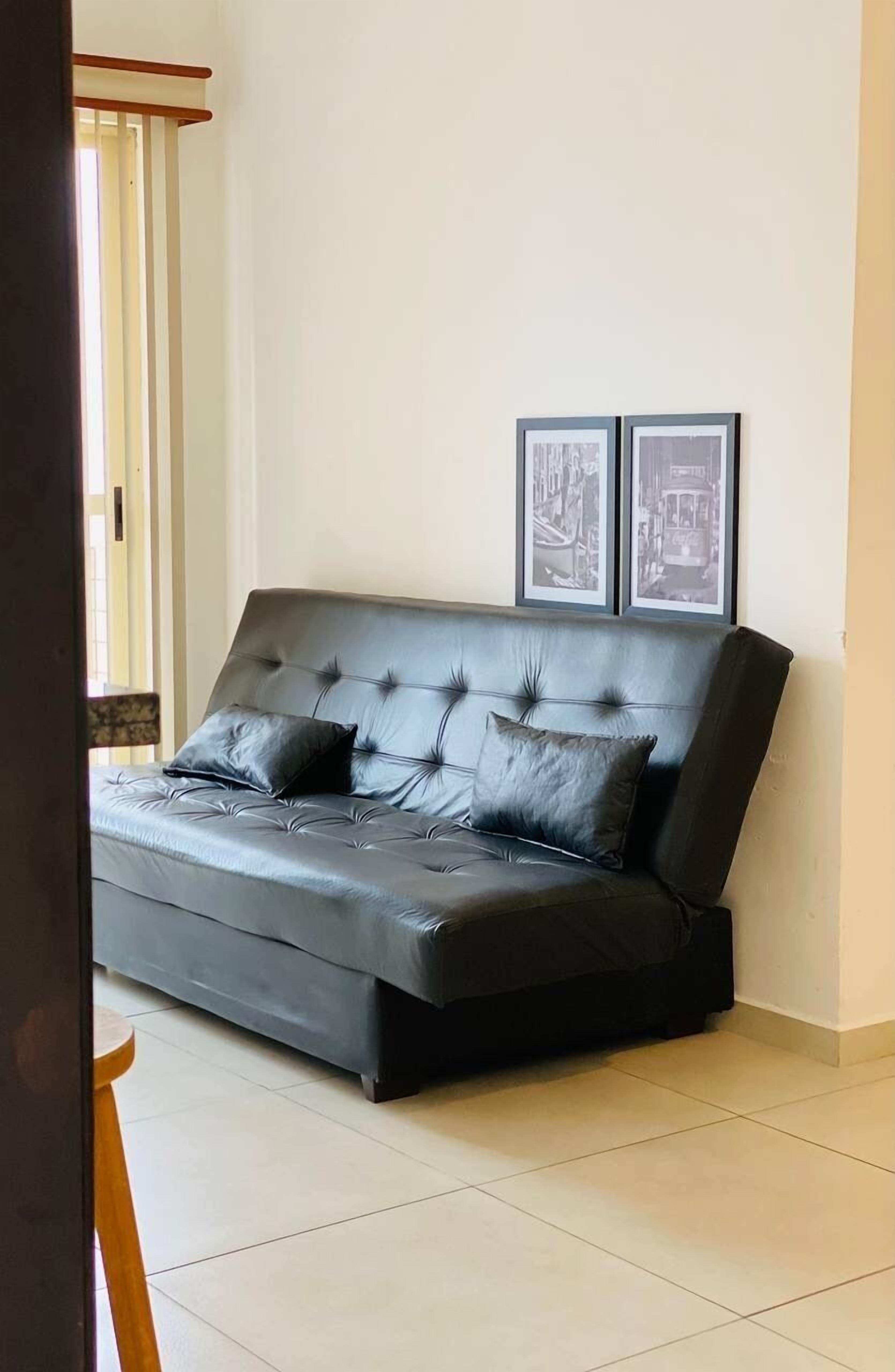 Una sala moderna con un sofá de cuero oscuro, dos cuadros enmarcados en la pared y piso de madera.