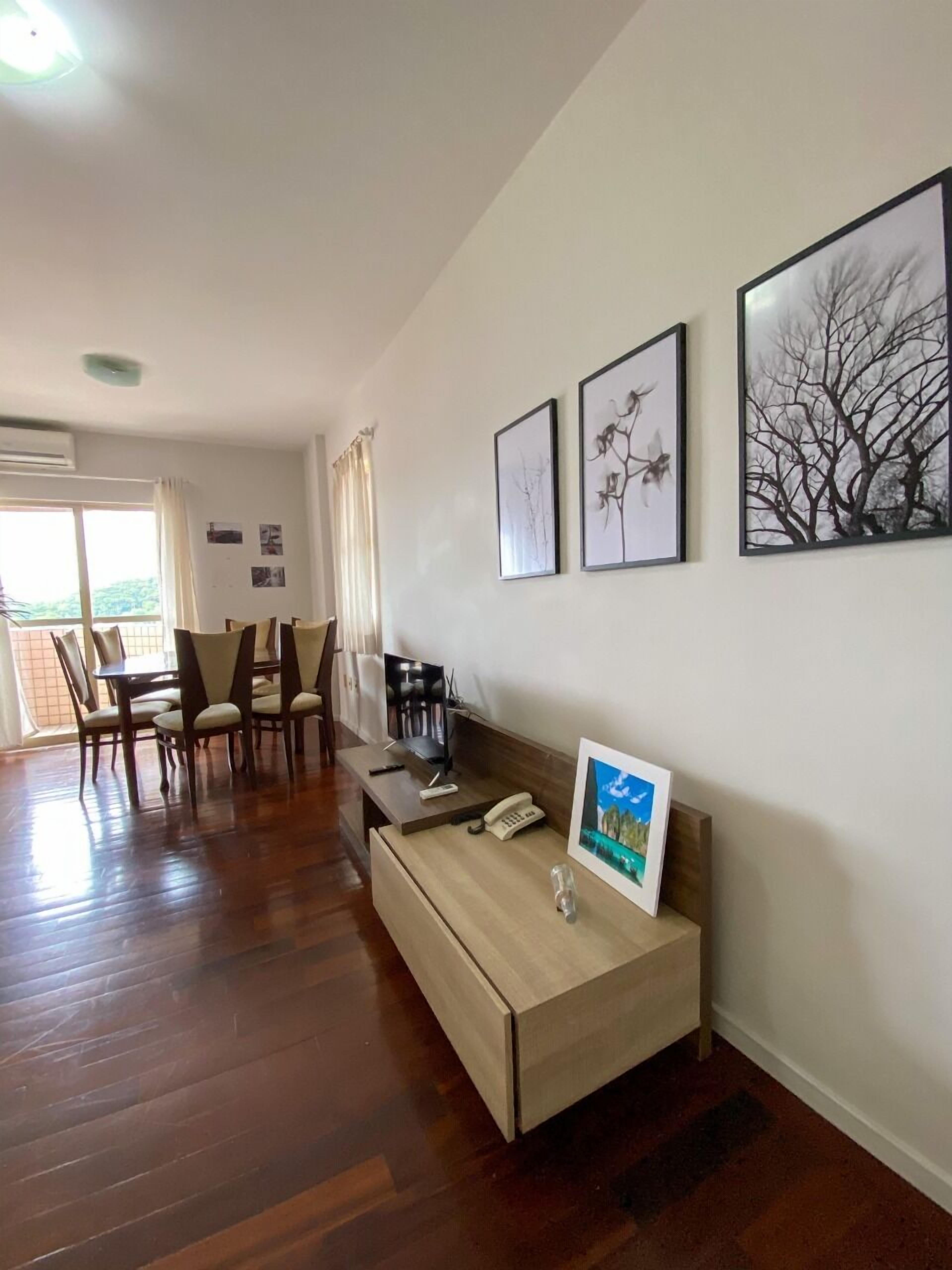 Un salón espacioso con suelo de madera, una mesa de comedor con sillas y un sofá con una mesita. Hay tres cuadros enmarcados en la pared.