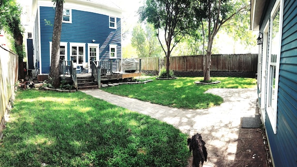 Un jardin avec un chemin dallé, une terrasse en bois et une maison bleue.