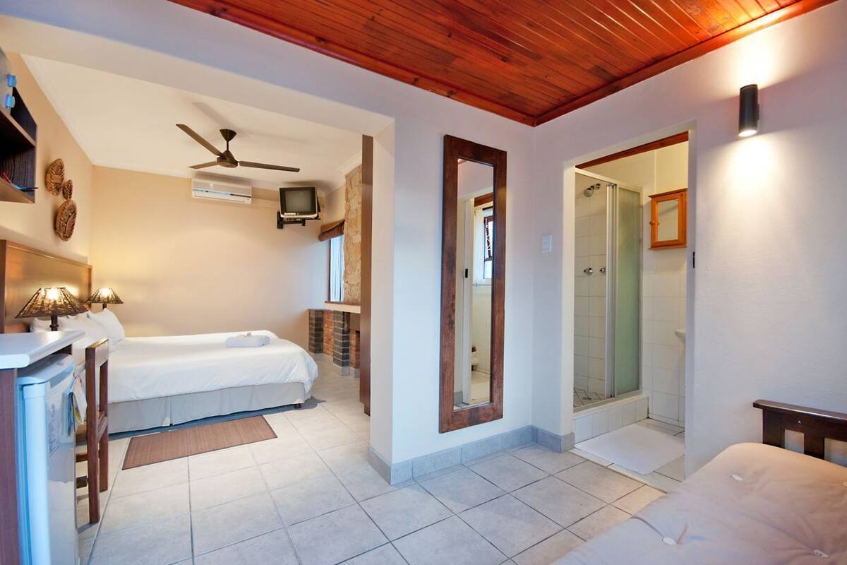 Un dormitorio con dos camas, ventilador de techo, televisor y zona de ducha.