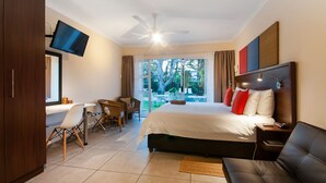 Habitación de hotel con cama, escritorio con silla, televisión montada en la pared y ventilador de techo.